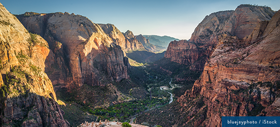 A view high up view of Zion National Park, mountains standing tall with a lush green valley and river winding between them