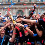 Players reach for the World Cup as confetti rains on them during a parade.