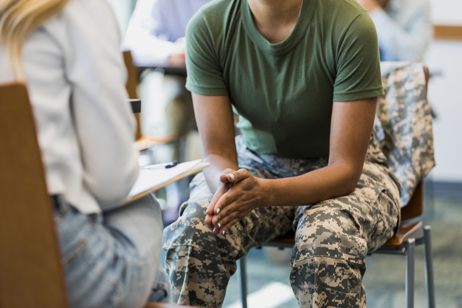 A close up photo of an unrecognizable mid adult female soldier as she puts her hands together and leans forward in her seat.