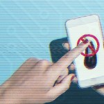 A hand with red-painted nails is holding a smartphone, and another hand is pressing a finger against the screen. The phone displays a red prohibition symbol (a circle with a diagonal line through it) over an eggplant emoji.