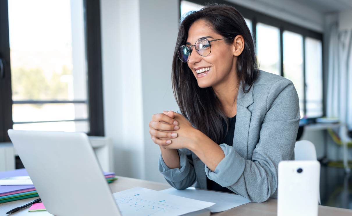 A woman in an office smiles as she looks at her laptop.