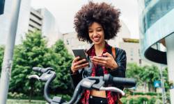 Smiling woman holding credit card while using mobile phone in city