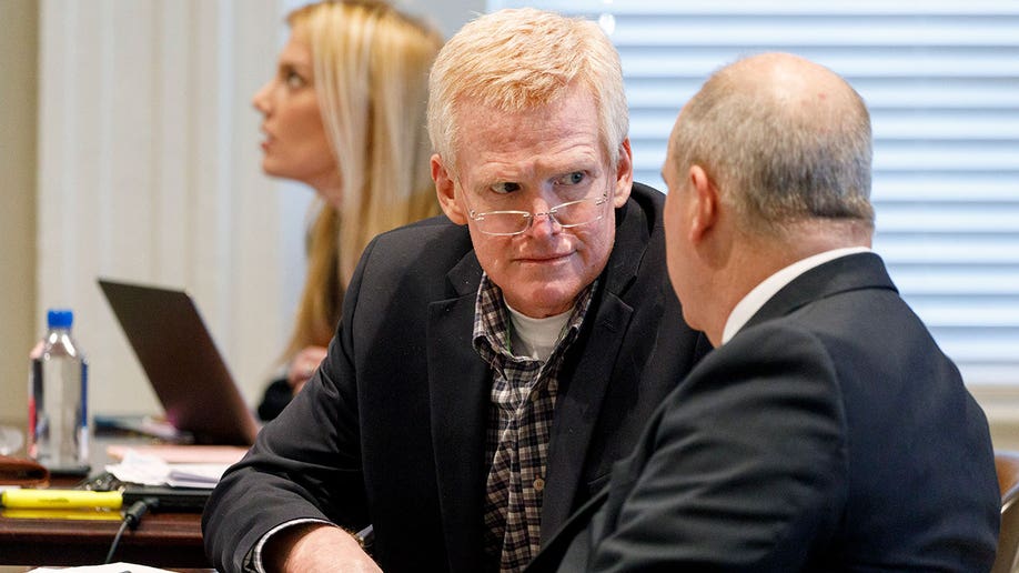 A man wearing glasses and a suit speaks to another man inside a courtroom.