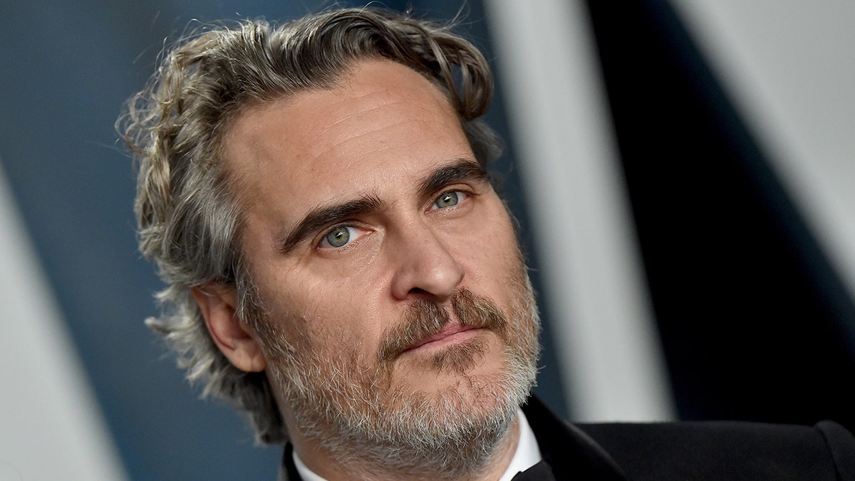 Joaquin Phoenix at the 2020 Vanity Fair Oscar Party on the red carpet in a black tuxedo looking off in the distance