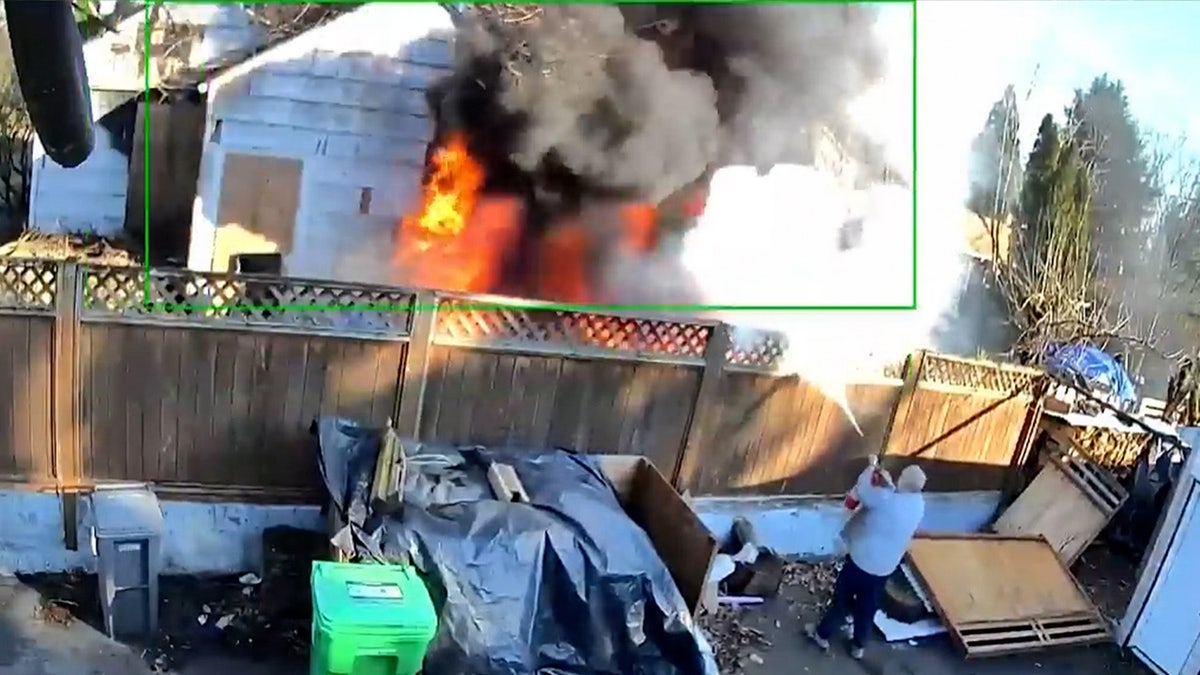 A person sprays a fire extinguisher over a fence at flames billowing from a Portland house