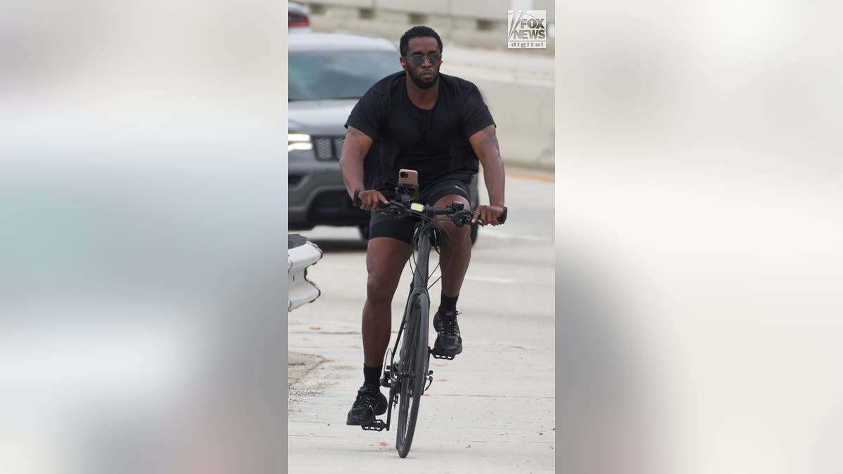 P Diddy looks at the camera wearing sunglasses as he rides his bicycle.