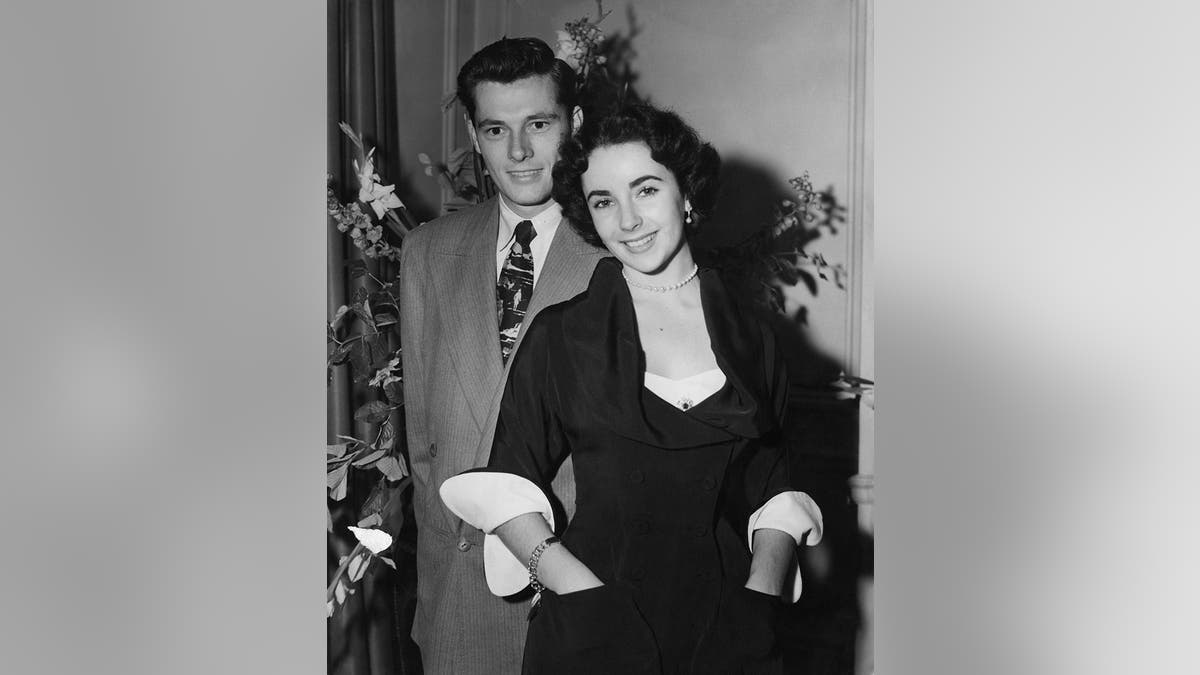 Elizabeth Taylor standing and smiling in front of Conrad Hilton