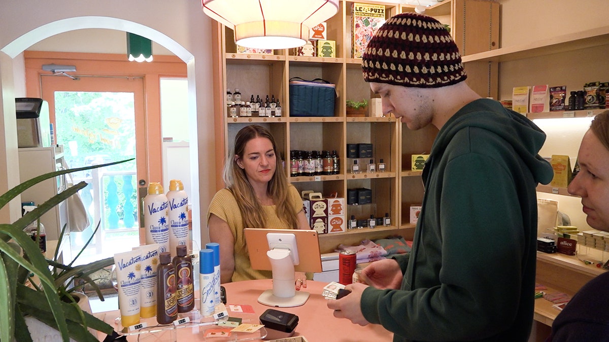 a woman checks some guys id at the checkout section of her NA bottle shop