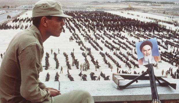 Guerra Irã-Iraque. Com uma foto do aiatolá Komehini na metralhadora, soldado iraniano vigia prisioneiros iraquianos