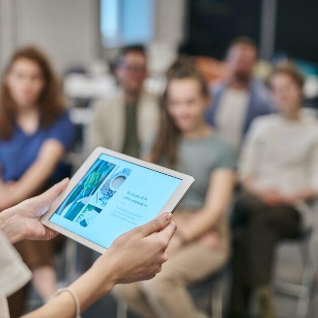 a person holding a tablet with a group of people sitting in rows in the background