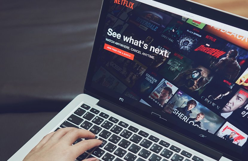 person types on computer that has Netflix home screen