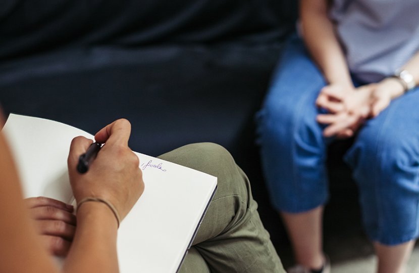 Photo of a person writing notes in a pad with a person sitting in front of them