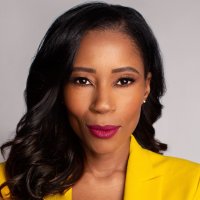 Woman in a deep yellow blazer stares directly at us with her arms crossed. 