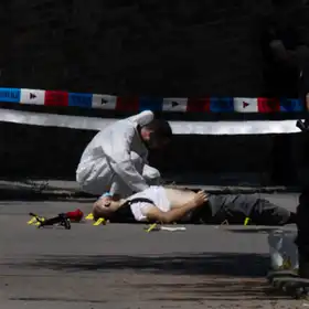 A forensic police officer inspects a body lying on the road next to the Israeli embassy in Belgrade (Photo by OLIVER BUNIC / AFP via Getty Images)