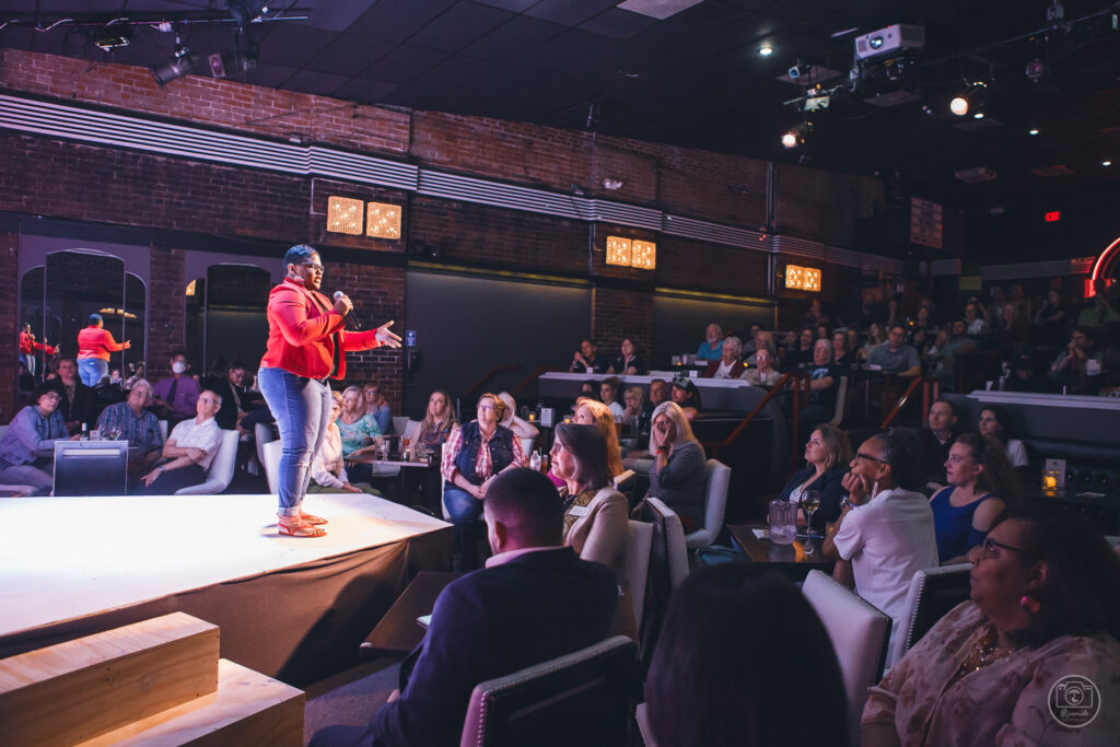 A person standing on a stage facing a large seated crowd.