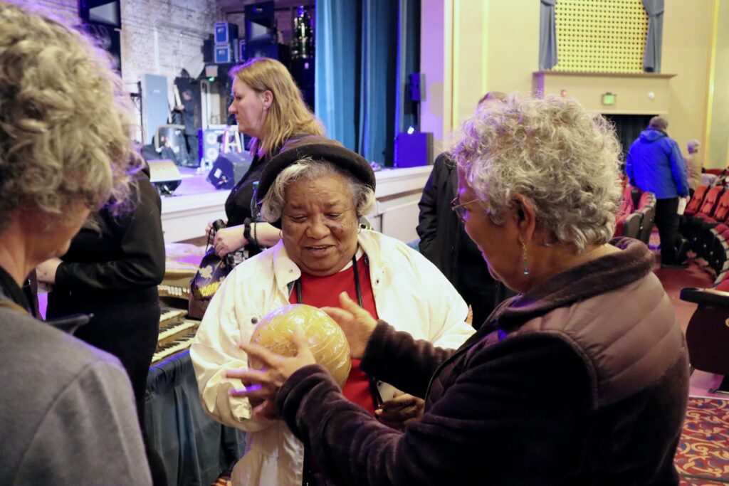 Two older adults hold a large, soccer ball sided shaker in their hands.