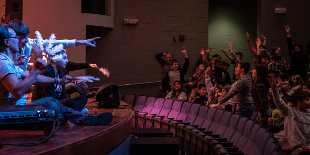 A group of musicians on stage interact with a group of students.