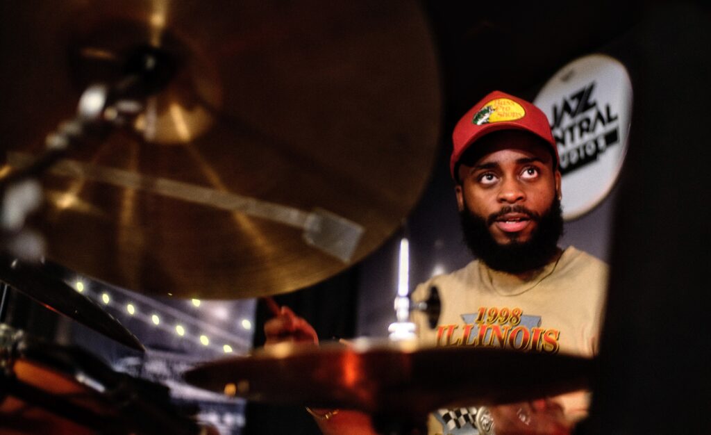 Jazz drummer playing a venue that has a sign that reads Jazz Central