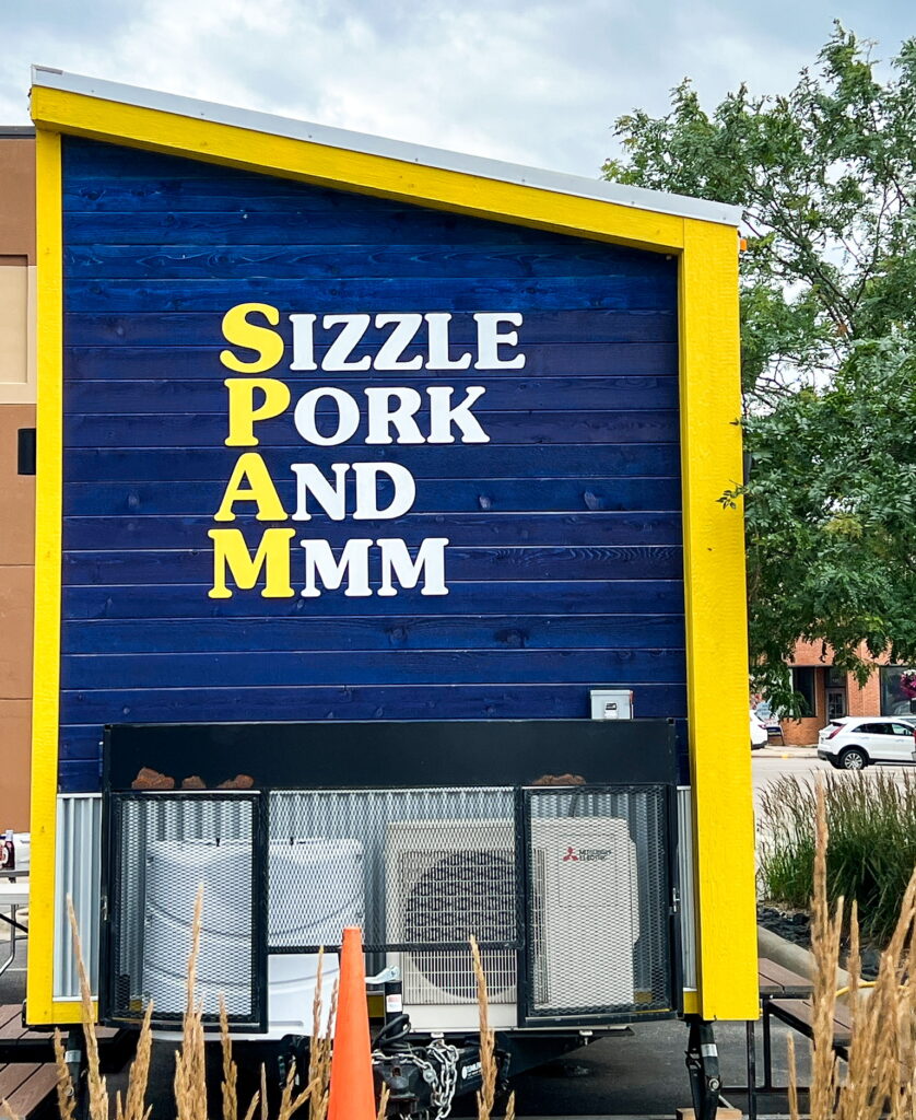 The side of a blue tiny house, with signage reading, "sizzle, pork, and mmm"