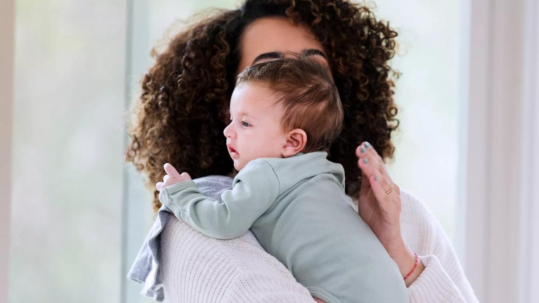 Caregiver burping baby, holding baby over their shoulder, patting baby's back