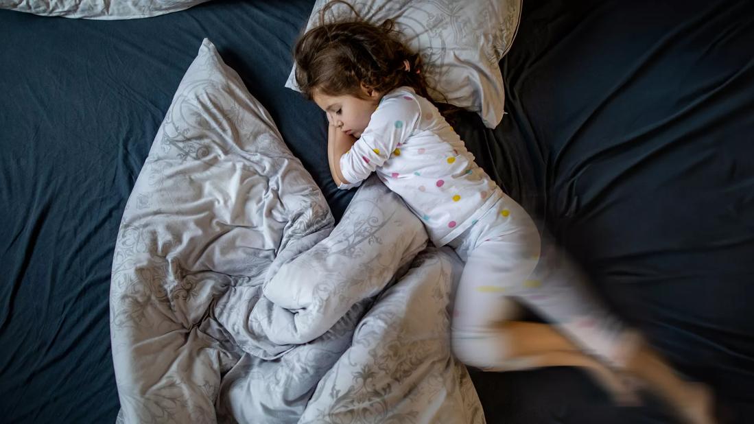 Child in pjs sleeping in bed moving legs