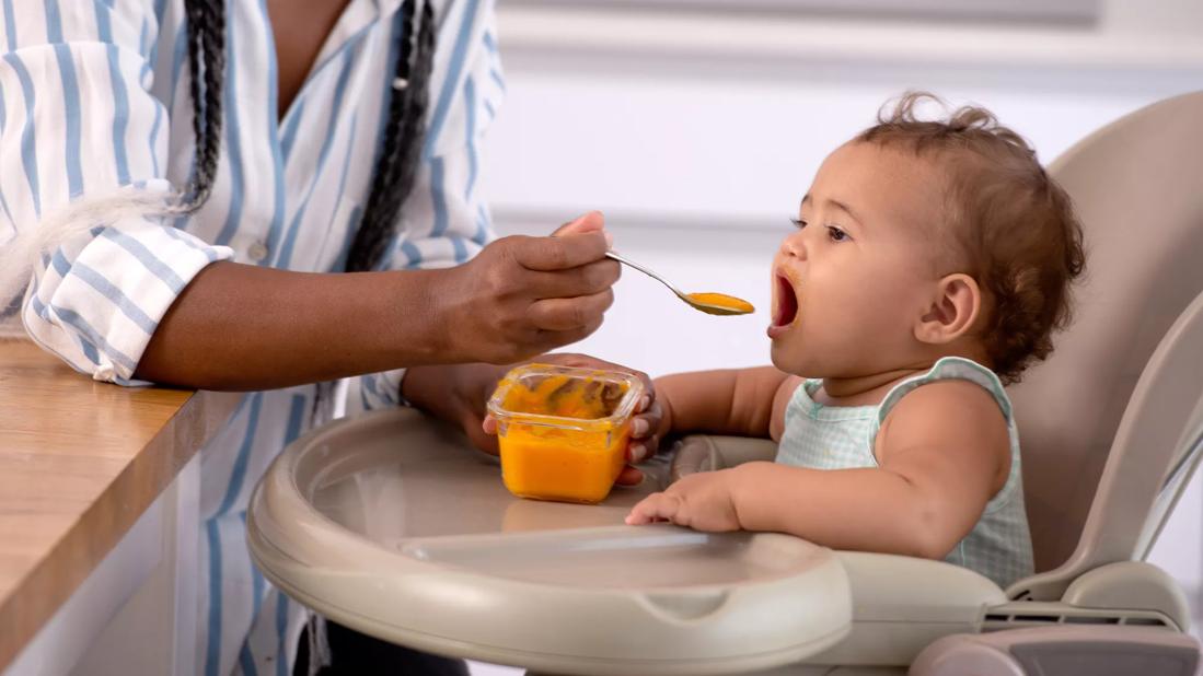 Caregiver feeding baby food to child in highchair