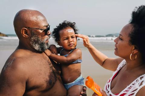 Parents applying sunscreen to their toddler at the beach