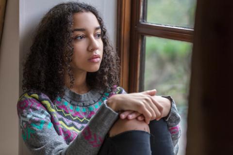 Teen sitting in window well staring out the window