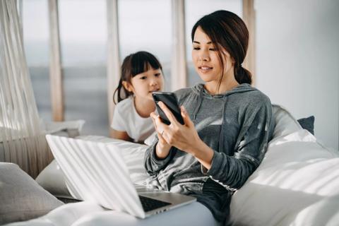 Child watching caregiver posting on phone and laptop