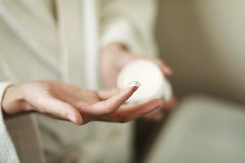 Person holding jar of moisturizer, with moisturizer on fingers