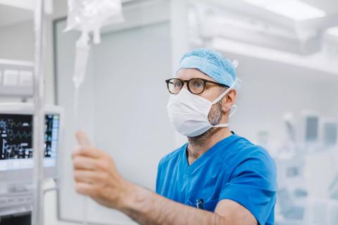 Healthcare provider in scrubs and mask in operating room checking IV line