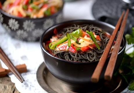 Black bean noodles with mixed veggies on top in a black bowl with chopsticks