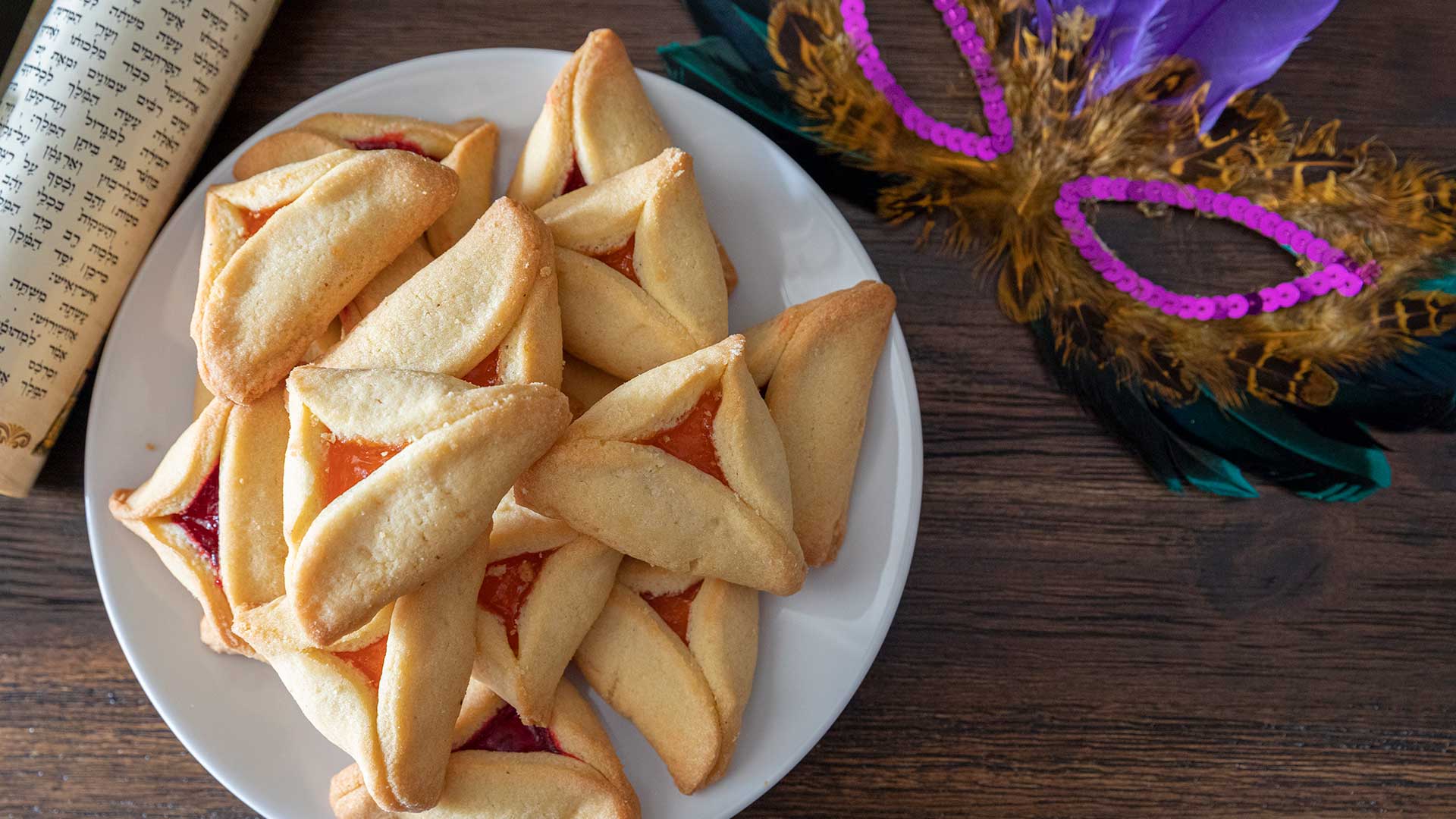 Hamantaschen on a plate with mask and Purim Scroll.