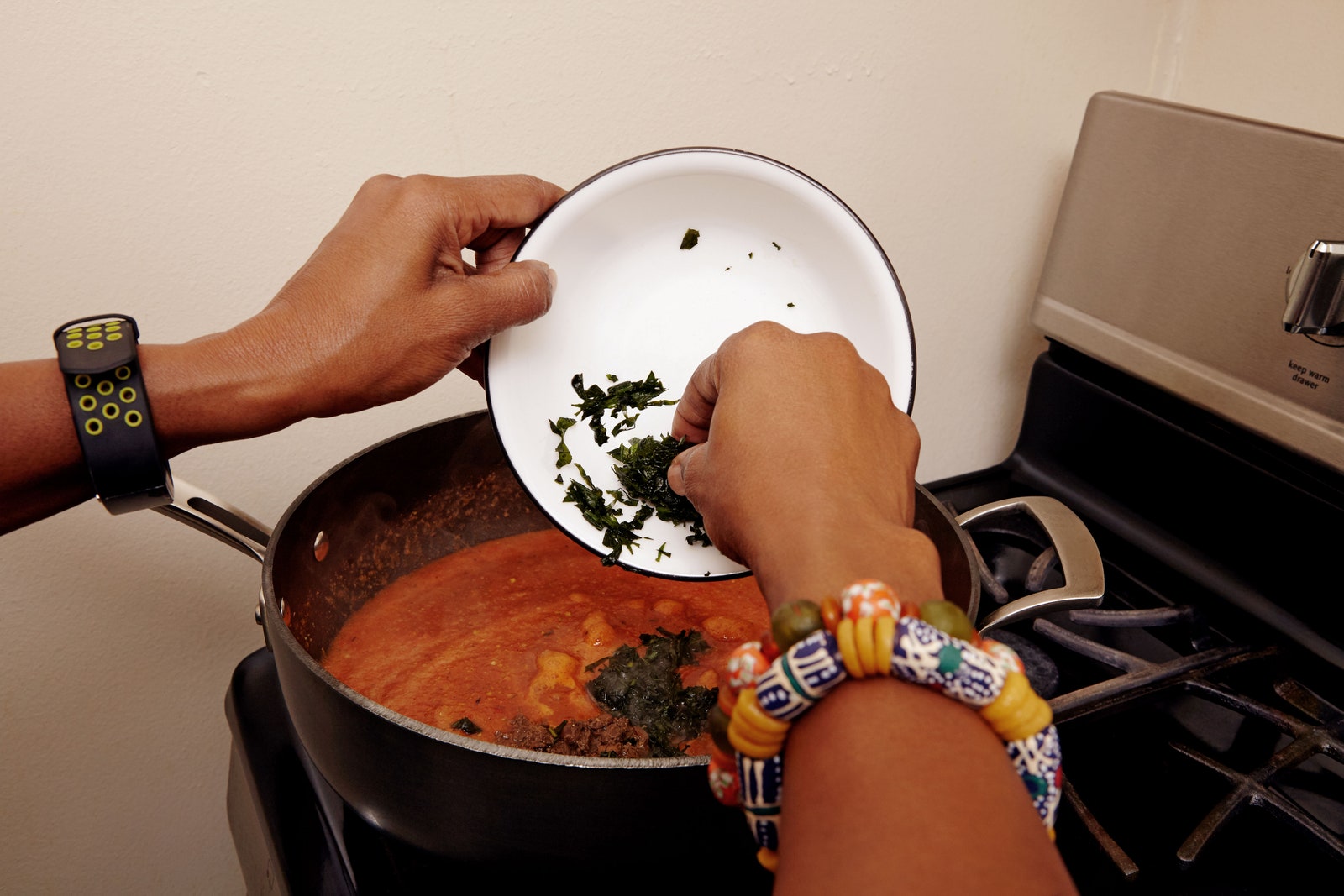 Photo of Kemi Seriki putting kale into Efo Iro on a stovetop.