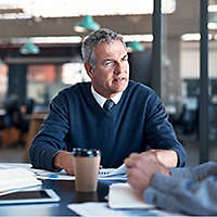 A business owner discusses succession planning with his partner at a boardroom table. 