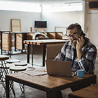 A man talking on his cell phone looking at something on his laptop computer.