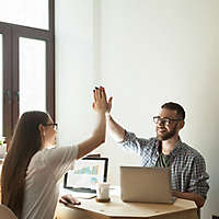 A young couple giving each other the high-five while working on their laptop computers.usiness deal.