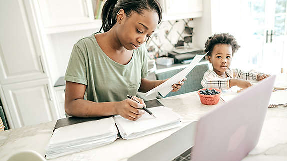 Mother doing paperwork; child in a highchair in the kitchen