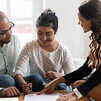 A couple at a table signing paperwork with an agent.