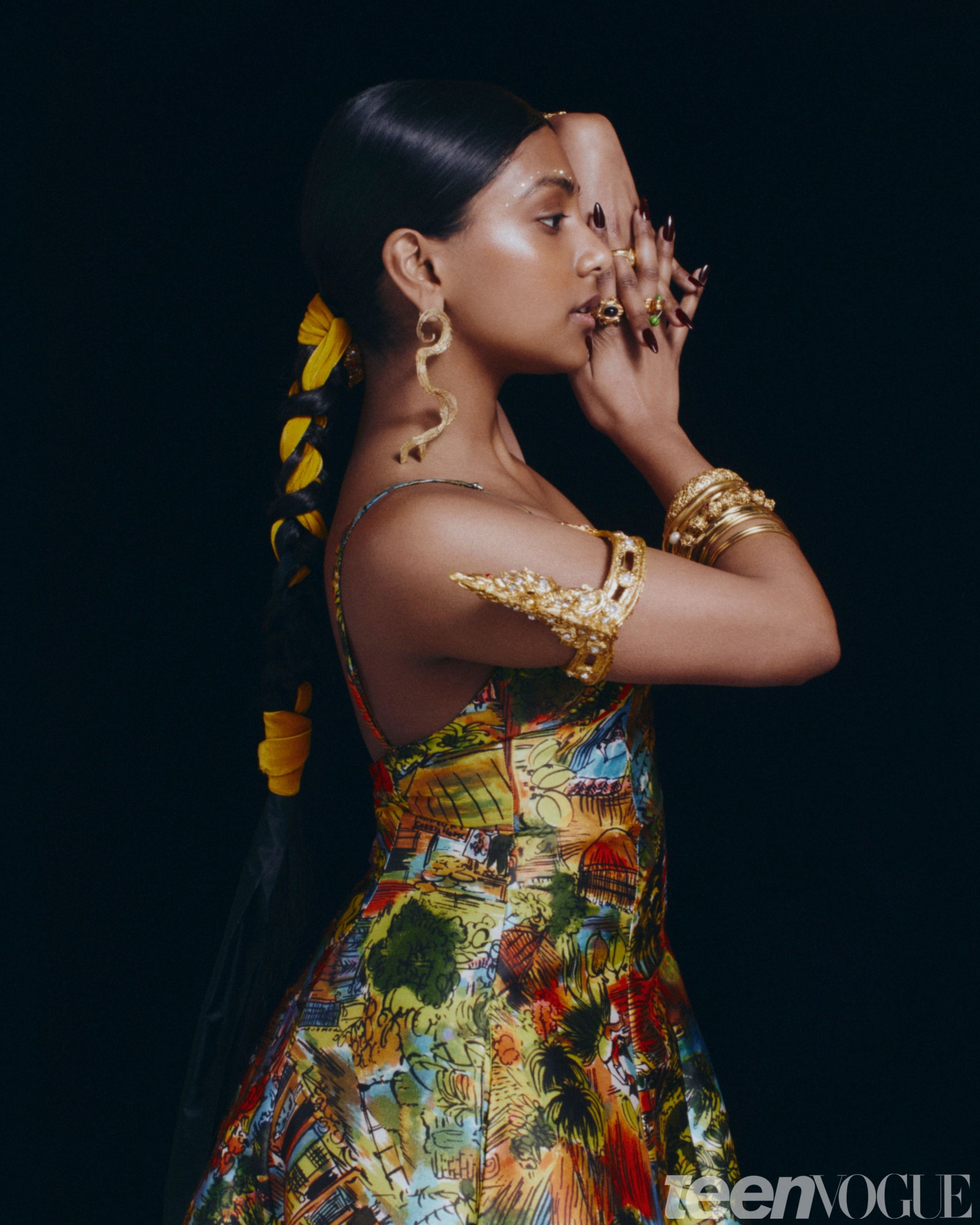 Charithra Chandran in profile wearing the same colorful dress and armbands she dons on the cover with her hands clasped...