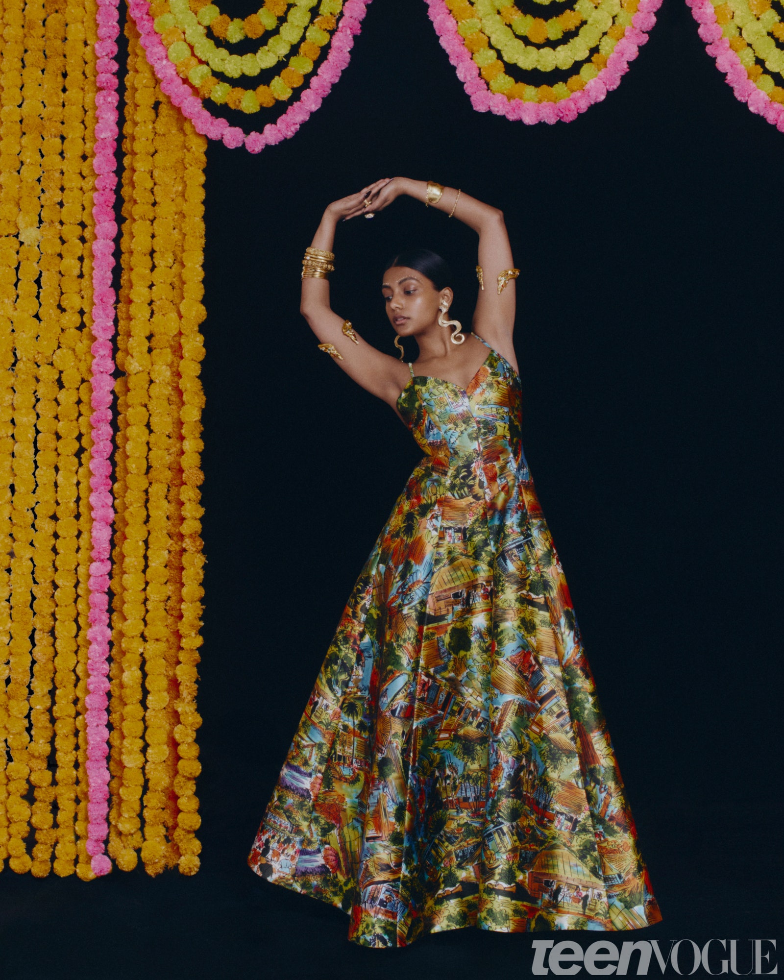 Charithra Chandran wearing the same colorful dress and armbands she dons on the cover standing in front of a black...