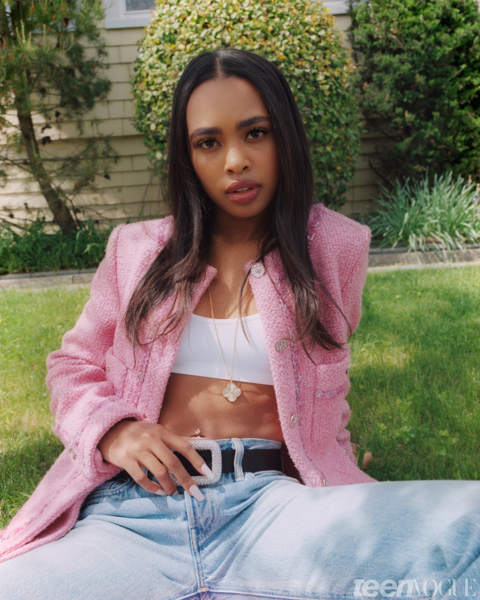 Zaria sitting outside on the grass in pink blazer and jeans