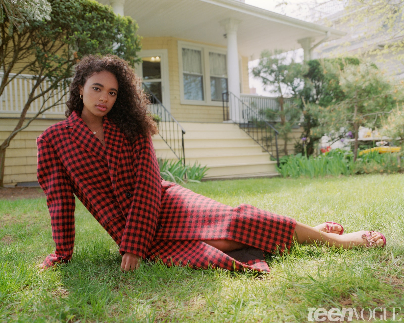 Chandler Kinney lounging on the grass in long red trenchcoat