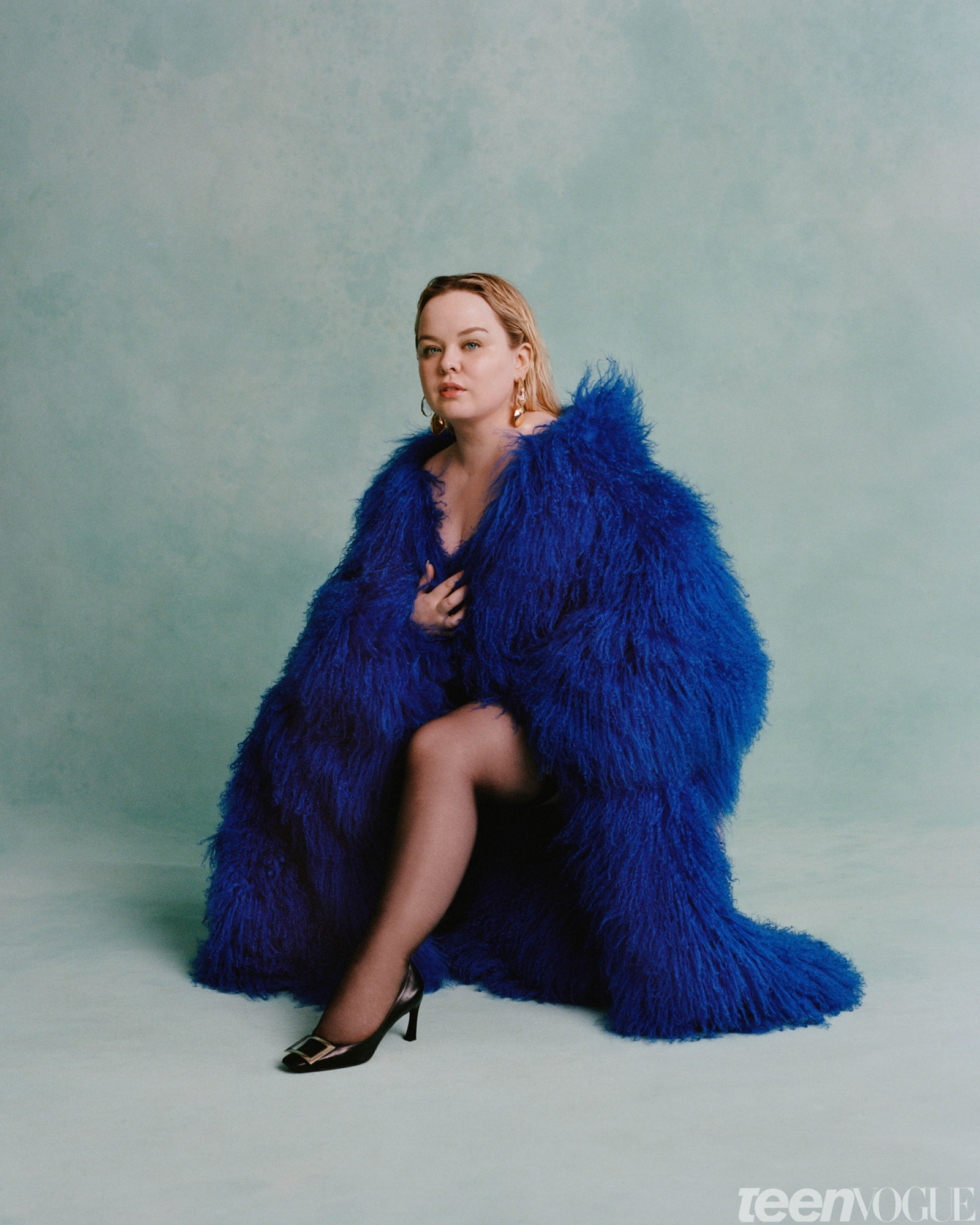 Nicola Coughlan kneelingin blue fur on a teal gray background