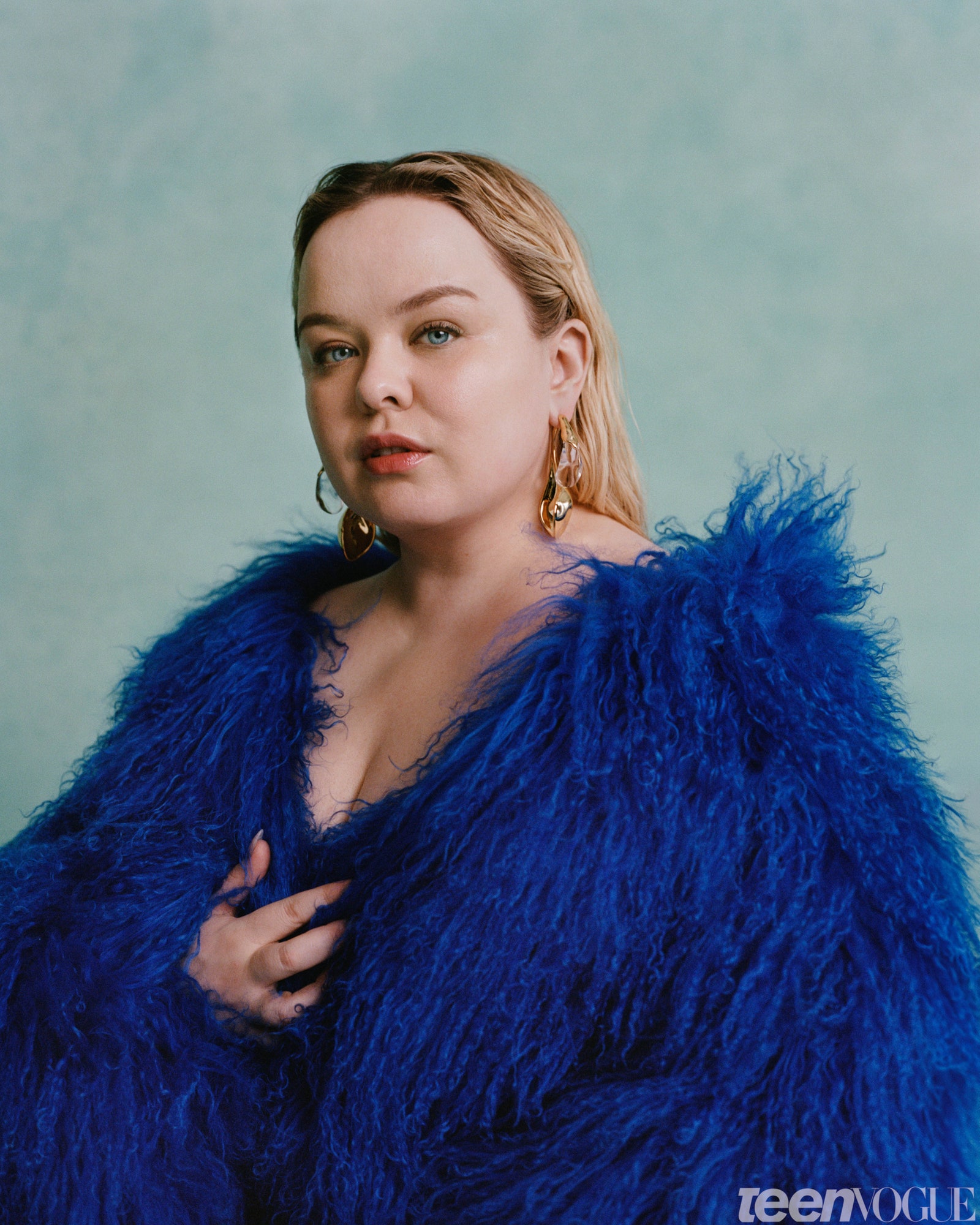 Nicola Coughlan kneeling in blue fur on a teal gray background close up