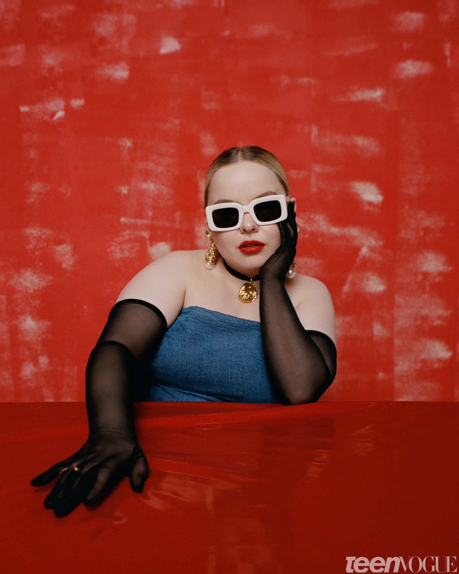 Nicola Coughlan with big sunglasses and gloves against a red backdrop