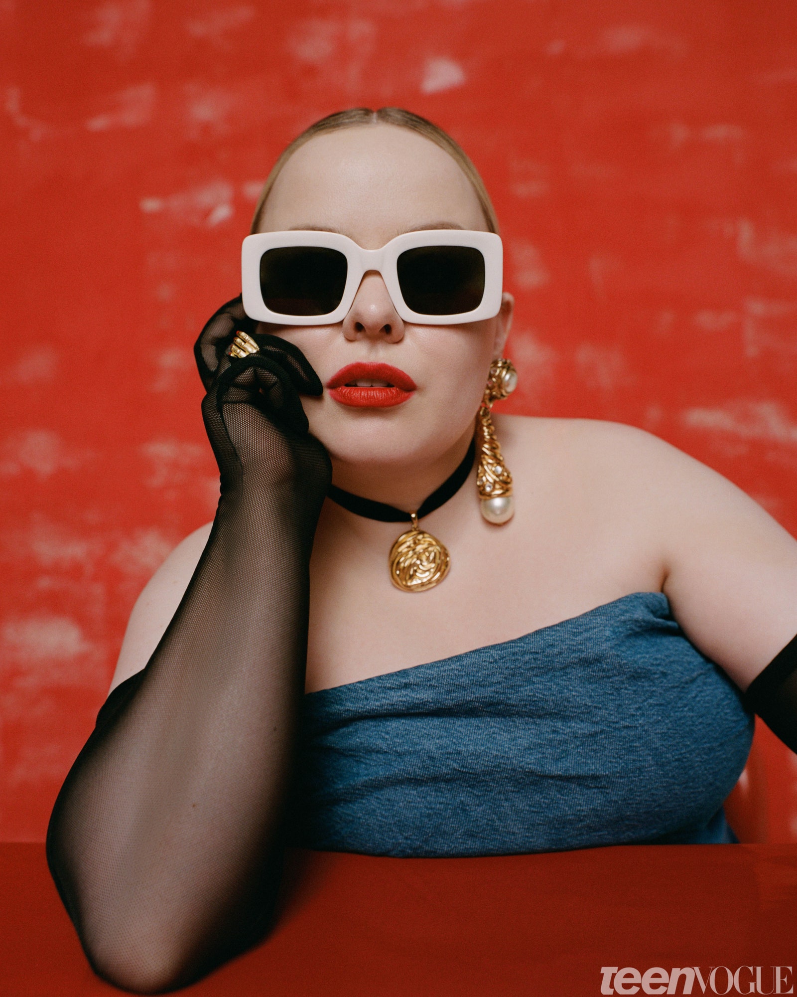 Nicola Coughlan with big sunglasses and gloves against a red backdrop