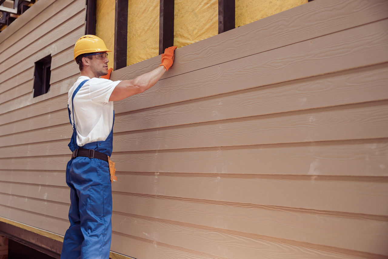 Handsome young man construction worker wearing safety helmet and work overalls while installing wood siding Male worker building house at construction site