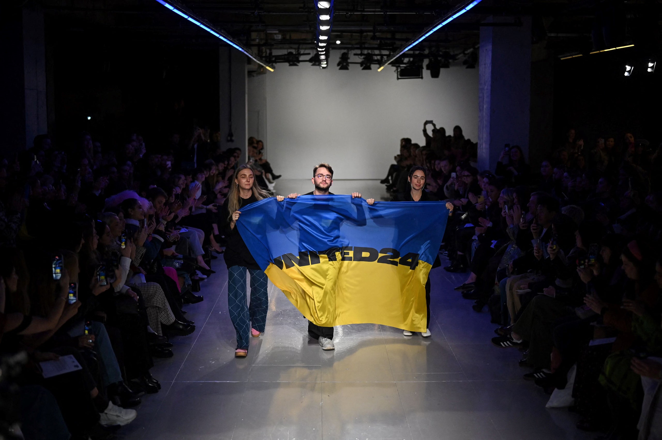 Designers Ksenia Schnaider Ivan Frolov and Julie Paskal carry the flag of Ukraine following their shows at London...