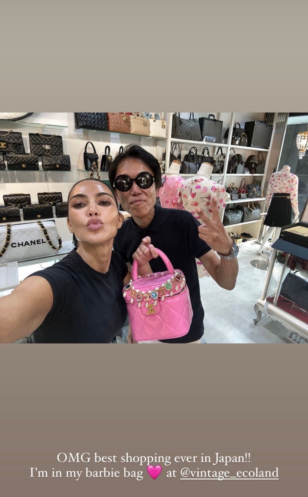 Kim Kardashian holds up a pink square purse with a pearl and crystal necklace draped over the top. She is with a man in...